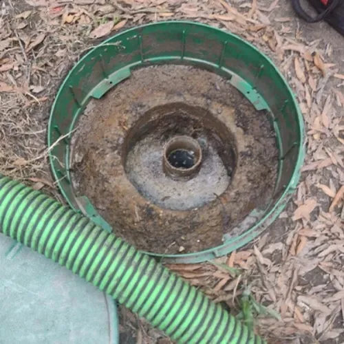 Green suction hose beside a cleaned septic tank riser and outlet baffle