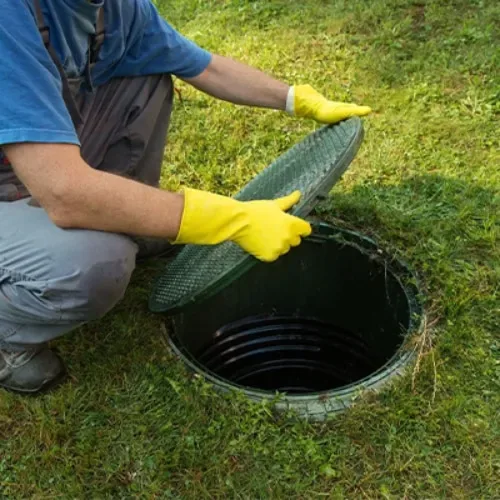 Technician lifting a septic tank lid to inspect sludge levels before installation work